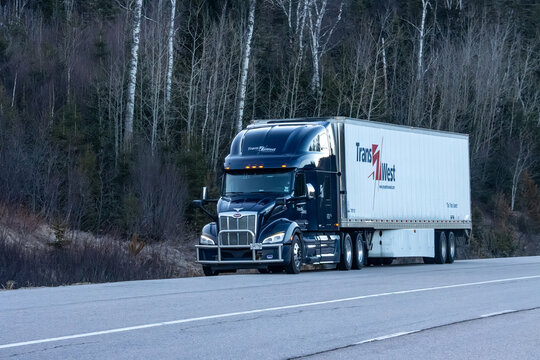 Quebec, Canada, 24 April 2026 : A dark blue Peterbilt semi-truck with a white TransWest trailer drives on a highway next to a forest.