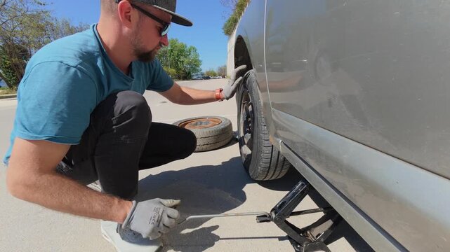 Man lifting a car with a scissor jack for wheel replacement