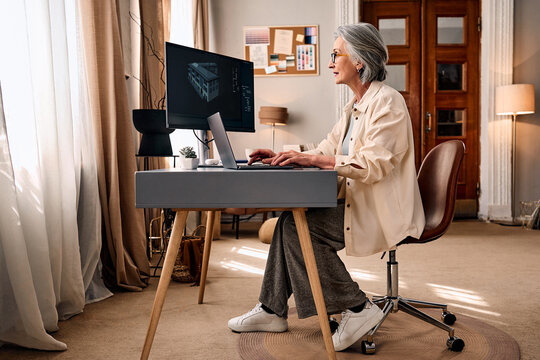 Senior woman working remotely at modern home office desk.