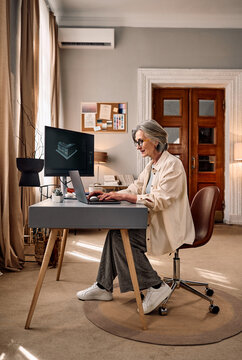 Senior woman working on laptop in modern home office.