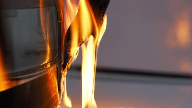 A electric kettle engulfed in flames, with the fire brightly illuminating its surface and rising upward. a dangerous situation, with dense tongues of fire covering its body.