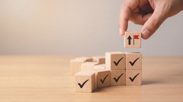Hand placing final block with arrow and flag on check-marked stack, symbolizing goal achievement and progress.