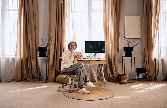 Senior woman working from home office with coffee and computer.