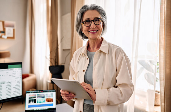 Senior businesswoman holding tablet in bright home office.