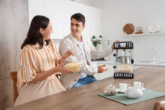 Cute couple with modern machine for making popcorn in kitchen