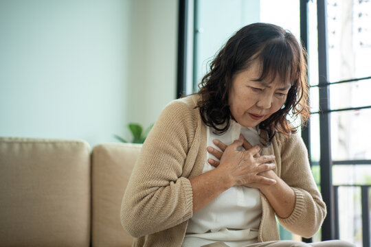 Unhappy Asian senior woman coughing with illness and fatigue while sitting alone on living room sofa, healthcare and medical protection planning for life insurance in retirement age