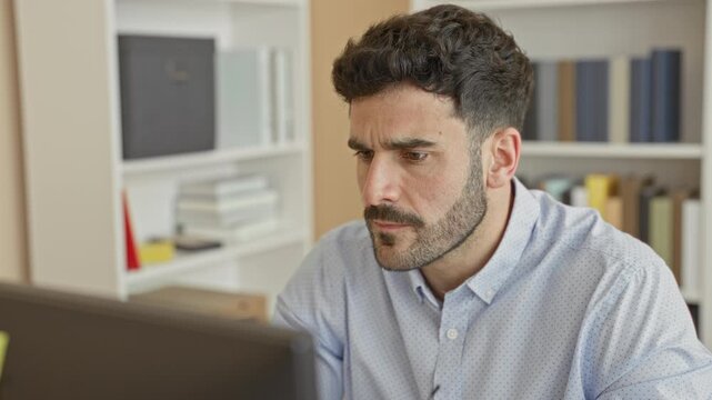 Man at computer monitor frowning and lifting glasses in office building; concentration problem solving.
