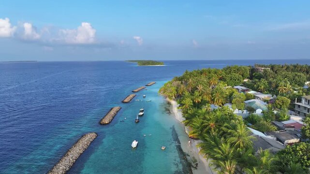 Aerial view of the lush tropical island of Kendhoo with palm trees, white sand beaches, and boats anchored in the turquoise lagoon, Kendhoo, Baa Atoll, Maldives.