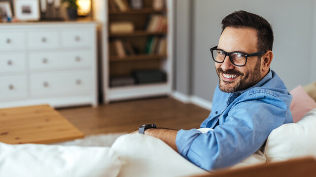 Smiling Man Relaxing on Couch at Home Looking Back Comfortably in Living Room
