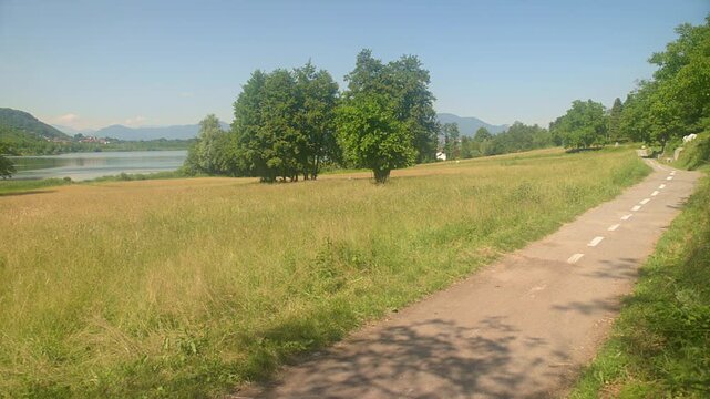 Man cycling away on lakeside path at lake Comabbio Italy, summer sunny day, rear view, fixed camera, outdoor sport, nature landscape, italian lakes lombardy