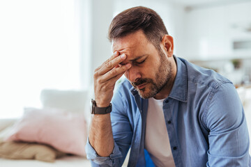 Stressed Man With Headache Rubbing Forehead While Sitting At Home Looking Tired And Worried