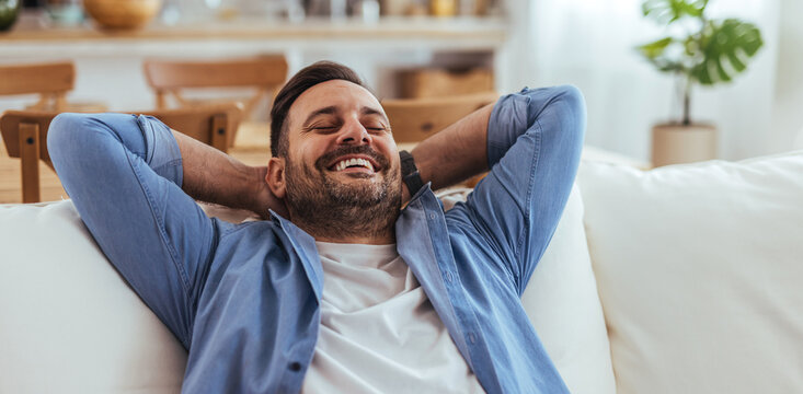 Relaxed Young Man Reclining on Sofa at Home, Smiling and Enjoying Leisure Time