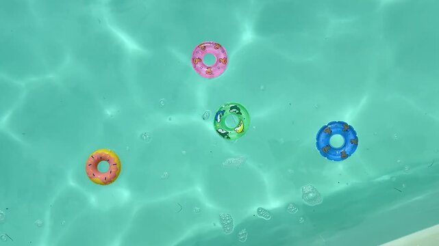 Overhead view of vibrant donut rings gently drifting in a sunlit turquoise swimming pool.