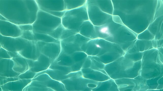 Blue swimming pool water with bright sunlight reflections creating shimmering ripples, top-down