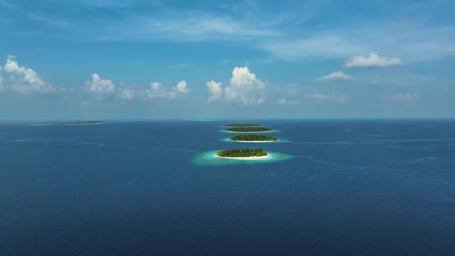 Aerial view of a chain of lush tropical islands surrounded by turquoise coral reefs and deep blue ocean water in Kendhoo, Baa Atoll, Maldives.