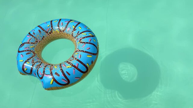Blue donut pool floats drifting across turquoise swimming pool water on a sunny day, top-down view