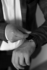Fototapeta premium Black and white close-up of a man in a checkered blazer adjusting his sleeve to check his wristwatch. A classic, formal shot of a groom or businessman preparing for an event.