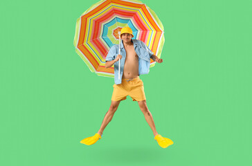 Happy young man in flippers with umbrella jumping on green background © Pixel-Shot