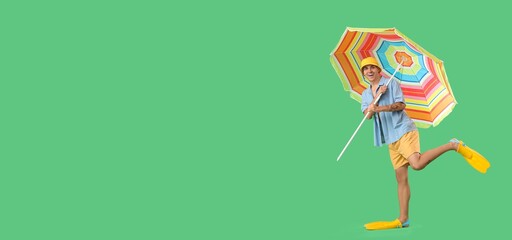 Happy young man in diving flippers and with beach umbrella on green background with space for text © Pixel-Shot