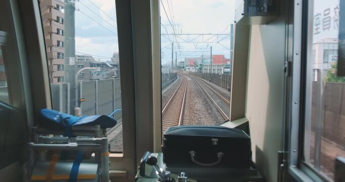 View thought, train driver cabin of fast moving in sunny Japan. Point of view from inside train operator cabin traveling on railway line through urban japanese landscape. Metro line rail in motion