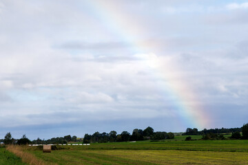 Naklejka premium Rainbow Over Green Rural Field with Hay Bales