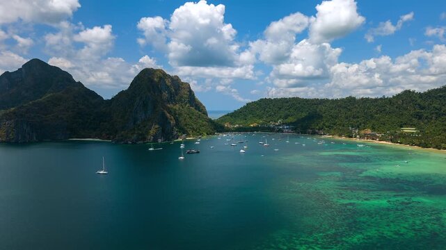 Timelapse aerial drone view of Corong Corong Bay in El Nido, Palawan, Philippines with turquoise sea, tropical mountains, anchored boats, and moving clouds above the coastline.