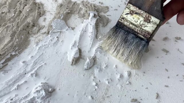 Static 4K close-up of a brush painting a textured cement wall art piece white. Minimalist DIY home decor project and creative process.
