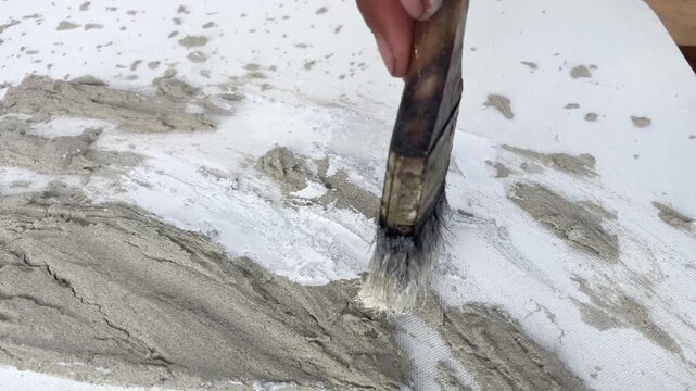 Static 4K close-up of a brush painting a textured cement wall art piece white. Minimalist DIY home decor project and creative process.