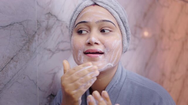 Young woman washing her face with foaming cleanser in bathroom, following daily skincare routine for clean and healthy skin.