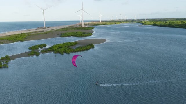 Kitesurfer riding in lagoon near Ilha do Guajiru Itarema municipality Ceara state Brazil with inflatable leading edge kite and wind turbines showing wind sport and energy landscape aerial tracking