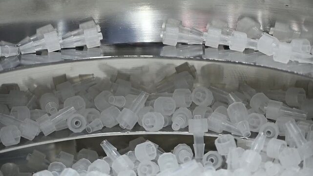 Automated blow feeder machine sorting clear plastic medical parts in a high-speed production line.