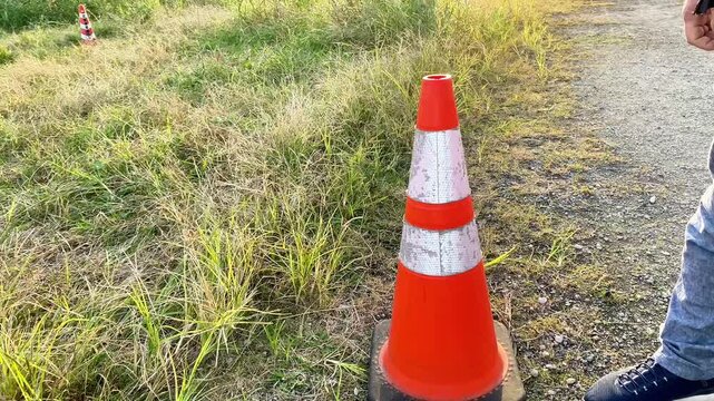 Main coup&eacute;e d'une personne pla&ccedil;ant un c&ocirc;ne de signalisation orange sur un chemin herbeux.