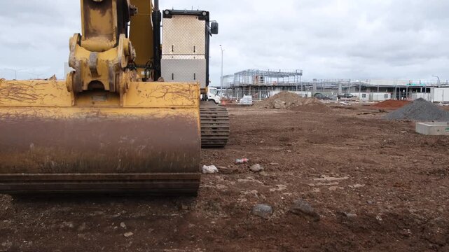 Soil mounds and construction site, early stages of urban infrastructure development with a large excavator bucket resting on the dry, unlevelled soil. Tarneit, Melbourne Australia