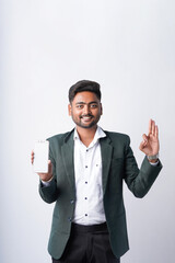 Fototapeta premium young indian businessman showing smartphone screen standing on white background
