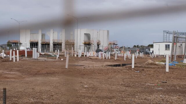 a modern civic or commercial building in Tarneit, Melbourne Australia. Unlevelled earth and several white PVC utility pipes protruding from the ground, precast concrete tilt-up panels being erected.