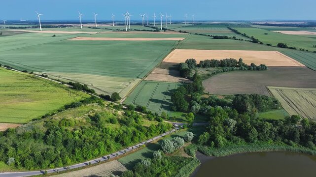 Aerial view of vast agricultural fields and a wind farm on the horizon under a clear blue sky in Uckermark, Brandenburg, Germany.