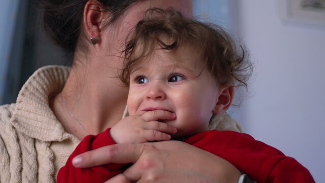 Mother kissing baby close up, infant reacts with wide-eyed surprise and open mouth expression, tender family moment of love and affection at home