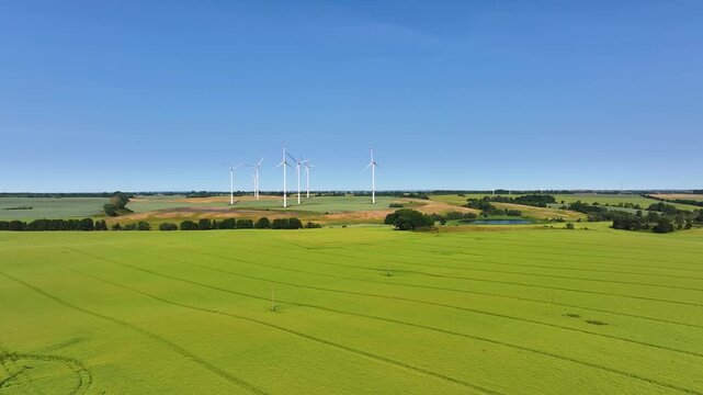 Aerial view of wind turbines standing in vast green agricultural fields under a clear blue sky in Uckermark, Brandenburg, Germany.