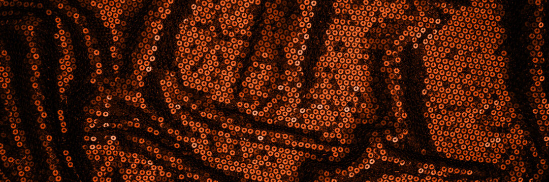 Artwork made from orange sequins arranged to form a detailed pattern on a dark background showing texture and design