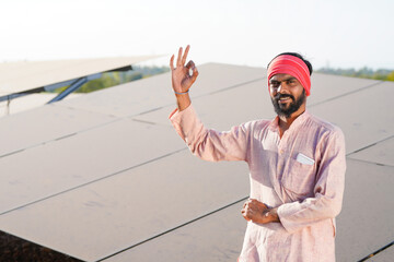 A confident indian farmer or rural worker stands in front of solar panels at agriculture field © PRASANNAPIX