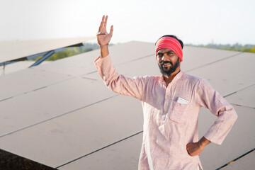 A confident indian farmer or rural worker stands in front of solar panels at agriculture field © PRASANNAPIX