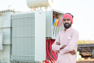 A power plant worker stands confidently in front of a large electrical transformer © PRASANNAPIX