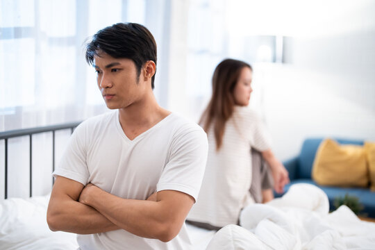 Upset Asian couple having relationship problems in bedroom, young man and woman ignoring each other after argument, emotional distance, marriage conflict and breakup concept at home