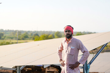 A rural worker stands proudly in front of solar panels giving a thumbs-up © PRASANNAPIX