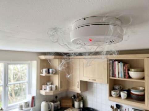symbolizing fire safety and early warning system. Ceiling mounted smoke detector emitting alarmed smoke in a home kitchen, 