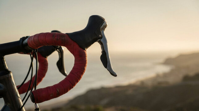 Road bike handlebars with red grip tape, close up of bicycle drop bars at sunset, cycling gear on coastal road background