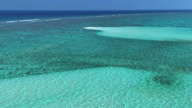 Aerial view of turquoise coral reefs, clear shallow water and sandbanks under a bright blue sky in Thoddoo, Alif Alif Atoll, Maldives.