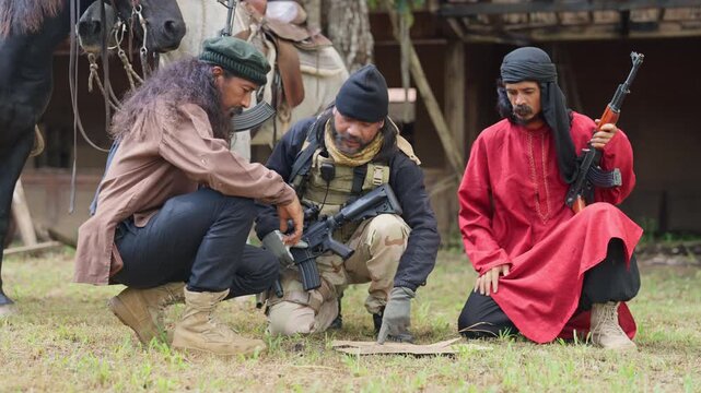 Group of men with soldier and arab clothes with gun stay on the ground and discuss about plan to fight with enemy.
