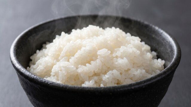 黒い茶碗に盛られた炊きたての白ごはんの接写、湯気と艶やかな米粒を強調した温かい和食イメージのクローズアップ