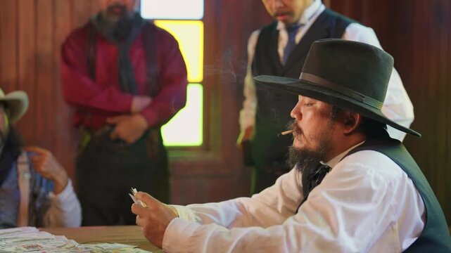 Young man with cowboy style is smoking during play card as gambling and the bodyguards stand around to protect member of gangster.